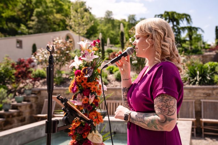 Ein lächelnder Mann in einem Anzug hält Spielkarten in einer eleganten Bibliothek.