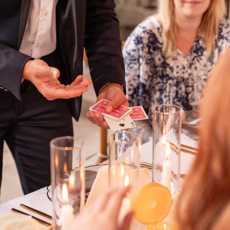 Ein Zauberer zeigt Karten während eines Abendessens mit Gästen.